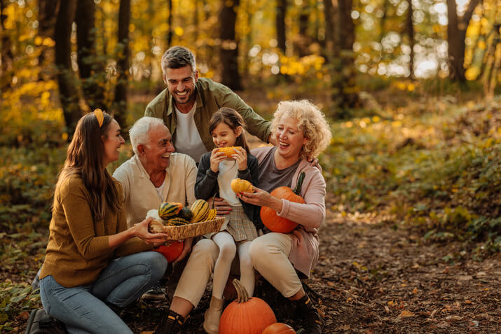Family laughing and smiling outdoors in autumn while holding pumpkins and gourds
