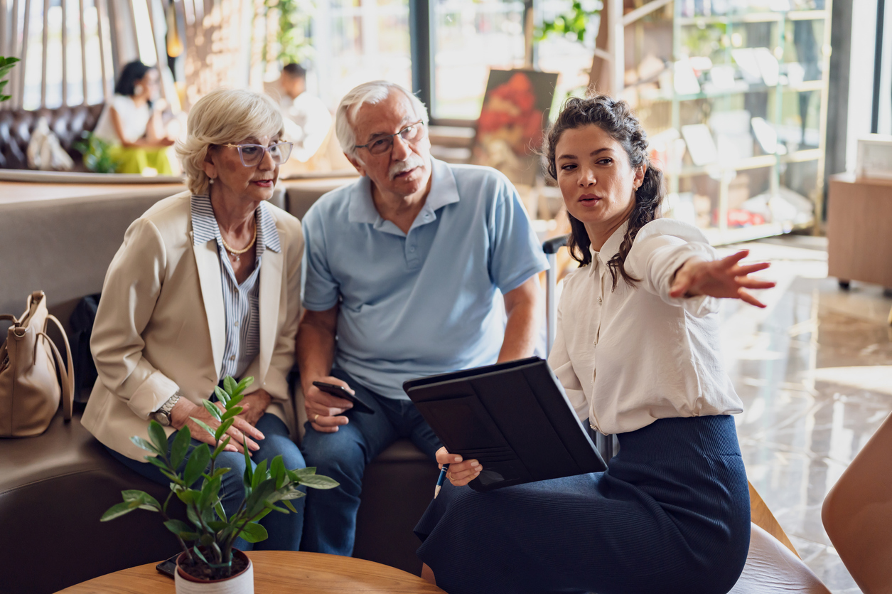 A hotel or travel agency representative is talking with a senior tourist couple offering various tourist services
